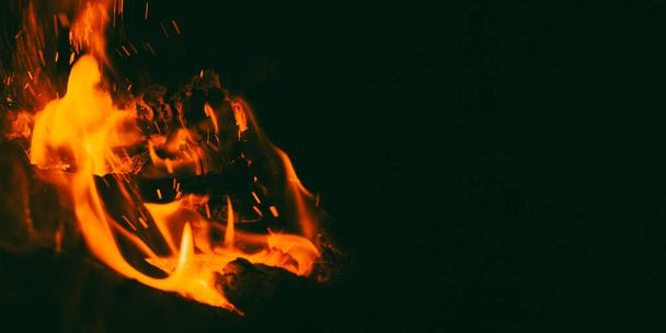 Burning wood in a campfire close-up. Selective focus. Charcoal in a bright red flame. Flashes and sparks in the fire of a forest fire. The concept of warmth and comfort. - Foto, imagen
