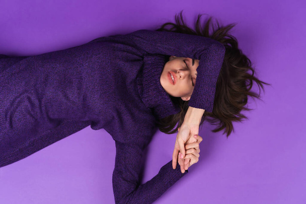Young woman in a knitted dress lies on a purple background - Φωτογραφία, εικόνα