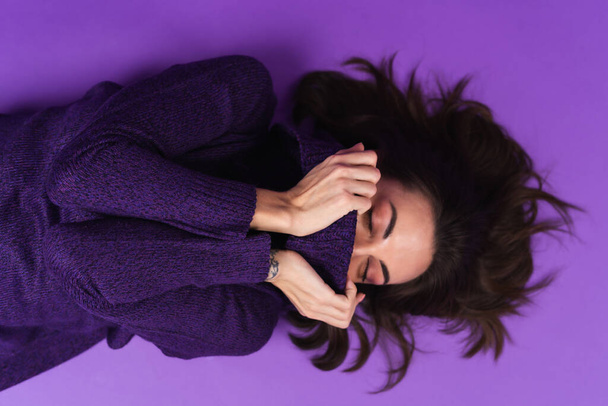 Young woman in a knitted dress lies on a purple background - Fotó, kép