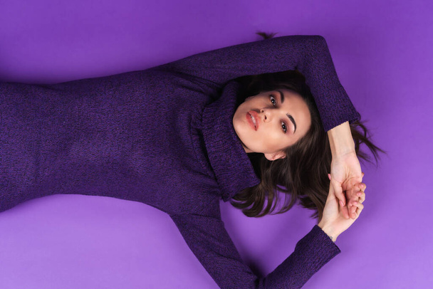 Young woman in a knitted dress lies on a purple background - Foto, imagen