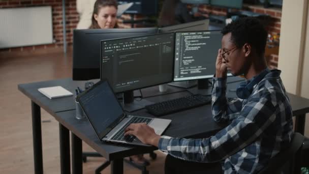 Retrato de programador cansado frotando los ojos mientras escribe en el ordenador portátil sentado en el escritorio con múltiples pantallas de análisis de código - Imágenes, Vídeo