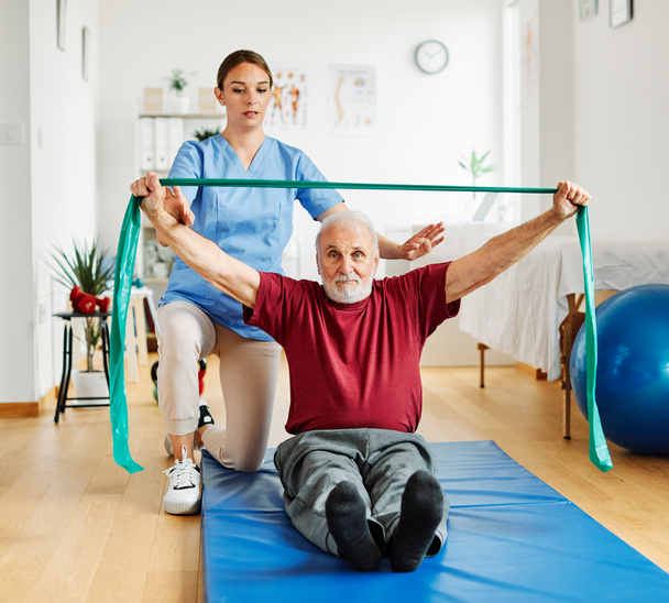 nurse doctor senior care exercise physical therapy exercising help assistence retirement home physiotherapy strech band clinic therapist elderly man - Zdjęcie, obraz