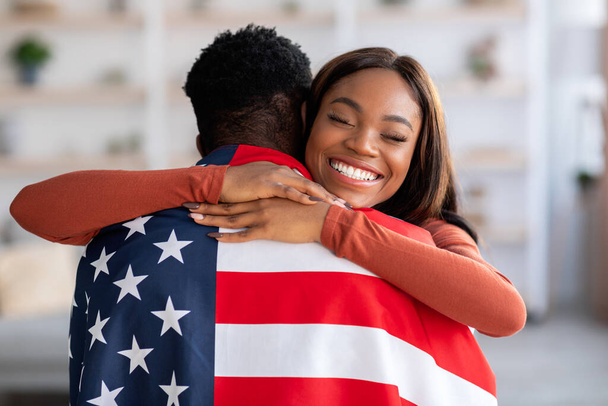 Independence Day. Happy Black Wife Embracing Husband Wrapped In American Flag - Foto, afbeelding