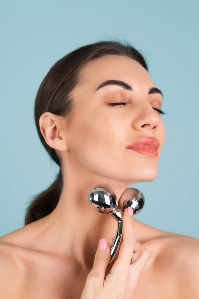 Close up beauty portrait of a woman with perfect skin and natural make-up, plump nude lips, holding a roller massager for face and neck - 写真・画像