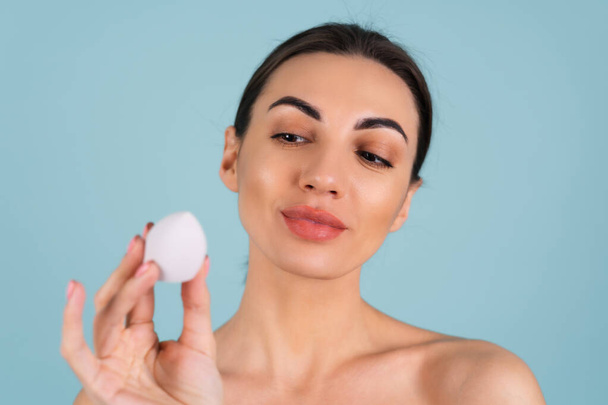 Close up beauty portrait of a woman with perfect skin and natural make-up, plump nude lips, holding a make-up sponge - Фото, изображение