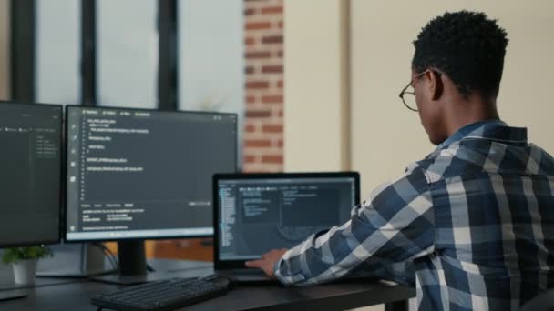 Focused software developer writing code on laptop looking at multiple screens with programming language - Séquence, vidéo