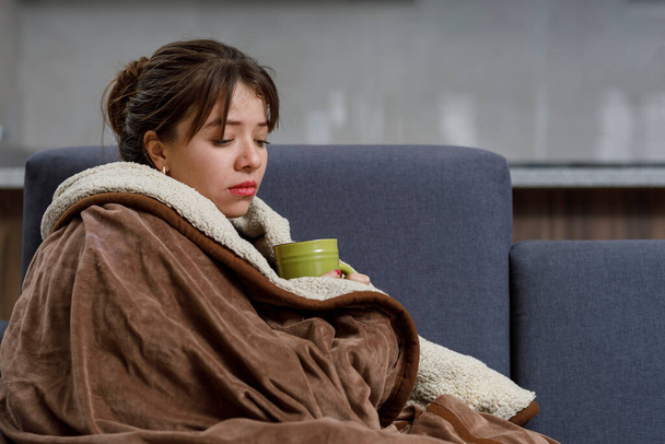Woman with a cup of tea, covered with a blanket, resting on her armchair for being ill - Photo, Image