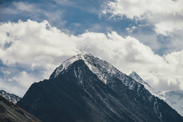 青空の下、山頂には雪が積もる高い山のシルエットを持つ大気中の高山風景。岩場の雪に覆われた山頂と高い雪の尖った頂点を持つ劇的な山の風景. - 写真・画像