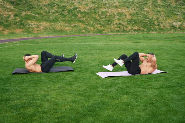 Two men with naked torso doing exercises for abs outdoors - Foto, immagini