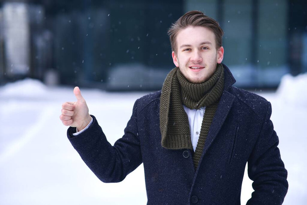 Portrait of handsome happy positive man, young successful businessman, blonde European man showing thumb up, like approval gesture, sign looking at camera at winter snowy day in snow in scarf smiling - Valokuva, kuva