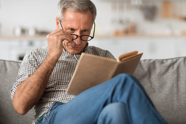 Senior Man With Poor Eyesight Reading Book Above Eyeglasses Indoor - Fotó, kép