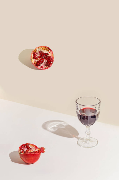 Creatieve compositie gemaakt van glas rode wijn of sap en granaatappels op pastelachtergrond met zonlicht. Zomer verfrissing concept. Minimale stijl. - Foto, afbeelding