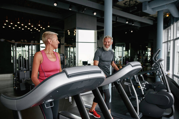 Aged couple exercising side by side in gym - Foto, afbeelding