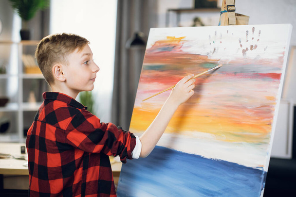 Caucasian boy using brush for painting on easel at sudio - Foto, afbeelding