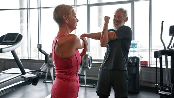Elderly man and woman stretching their arms at the fitness class - Photo, image