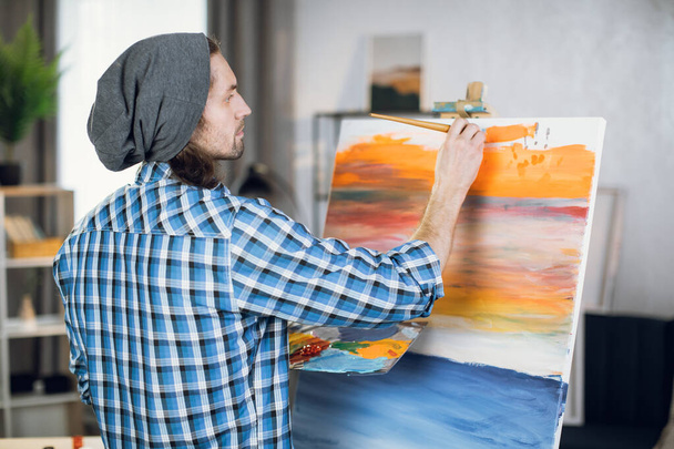 Man standing in front of easel and painting with brush - Foto, Imagem