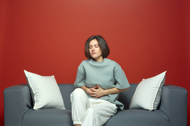 Unhealthy woman touch stomach suffer abdominal pain indigestion or menstrual period ach, sitting on sofa - Φωτογραφία, εικόνα
