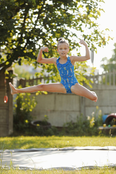 A kis sportos lány felugrik egy trambulinra. Szabadtéri felvétel egy trambulinon ugráló lányról, aki szeret otthon ugrálni. Boldog nyári vakációt!. - Fotó, kép