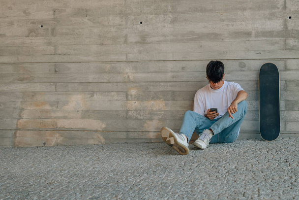 adolescente con teléfono móvil y monopatín en la pared - Foto, Imagen