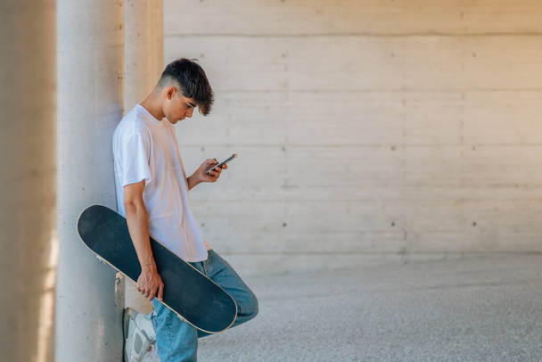 dospívající chlapec s mobilním telefonem a skateboardem - Fotografie, Obrázek