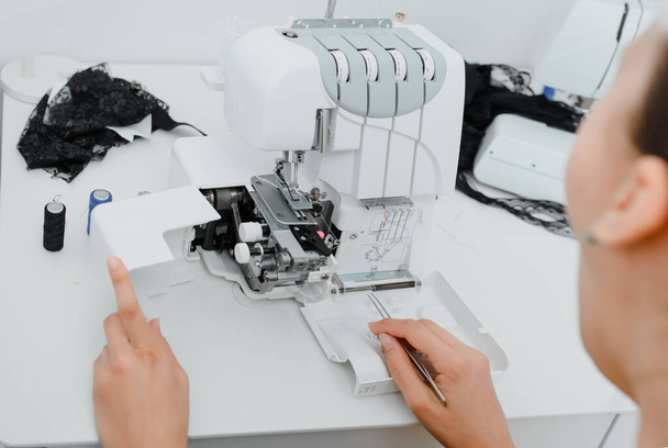 Interior of overlock machine/ serger concept. Female tailor is introducing thread to overlock machine/ serger on the table in her mini tailoring workshop. - Foto, imagen