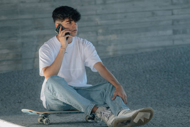 携帯電話とスケートボードを持つ10代の男の子 - 写真・画像