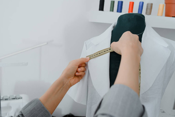 Young woman tailor is measuring with a centimeter ribbon a future shirt on a mannequin in her mini workshop - Foto, afbeelding