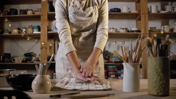 若い女性の陶芸家は、テーブルの上に粘土を置き、それを平らにするために圧延ピンを使用して - 映像、動画