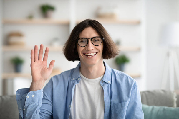 Greeting gesture concept. Happy young guy waving hand to camera and smiling, gesturing hi, making video call - Photo, Image