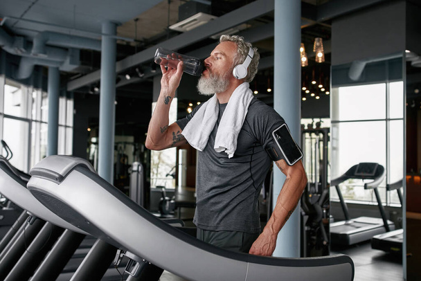 Senior man drinking water after running on treadmill - Photo, Image