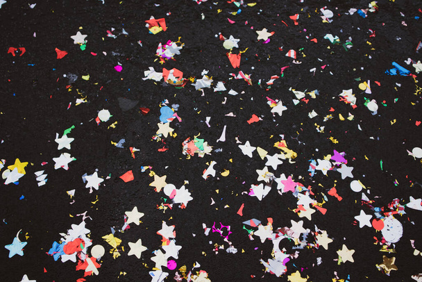 Party Poppers. Colorful explosion of holographic multicolored confetti lying scattered on a black surface. Bright multicolored tinsel, glitter, stars texture top view. Festive decoration background. - Photo, Image