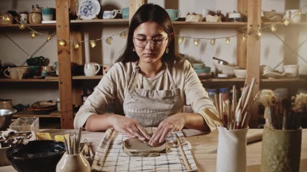 Young woman potter makes patterns of the piece of clay using stamping - Filmagem, Vídeo