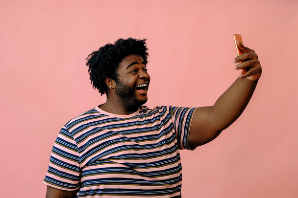 young african american man with a phone posing in the studio over pink background  - Фото, зображення