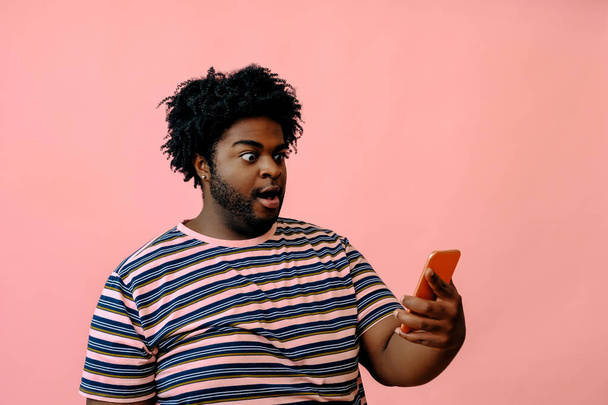 young african american man with a phone posing in the studio over pink background  - Fotoğraf, Görsel