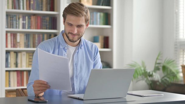 Succesvolle Man Lezen Documenten tijdens het gebruik van Laptop  - Foto, afbeelding