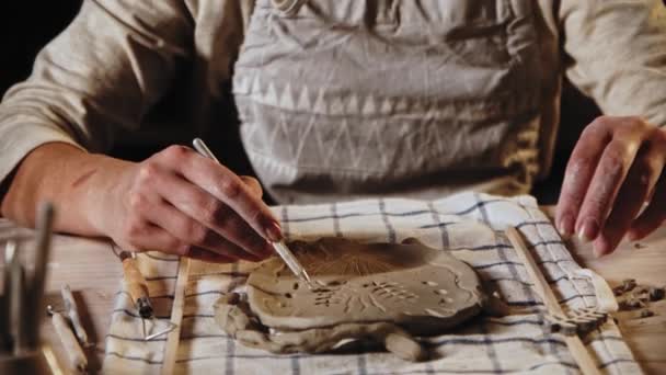 Young woman makes patterns on the wet clay plate using a tool - Filmati, video