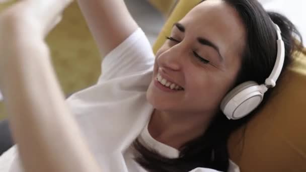 Happy woman listening music while sitting on couch at home - Filmagem, Vídeo