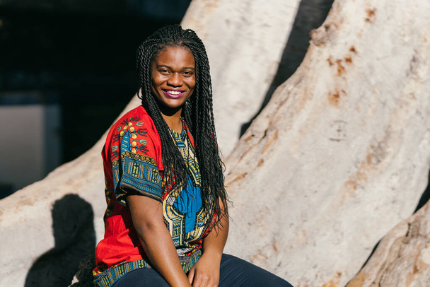 African woman in multicoloured ethnic clothing sitting in a park while smiling - Valokuva, kuva