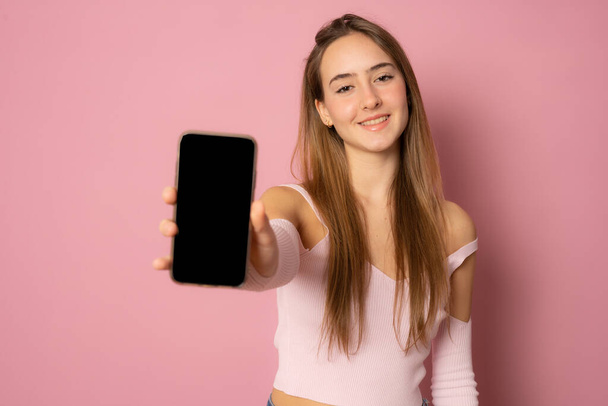 Close up portrait of young woman showing mobile screen over pink background. - Photo, image