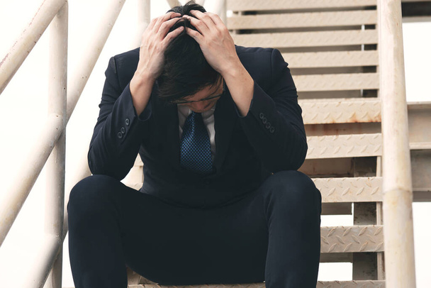 破産レイオフアジアのビジネスマンのストレス頭痛の階段のステップに座っている。悲しい失業者の痛みの不安アジアの人々の男性は、屋外に座って経済的な問題を悩ませた。失敗者概念. - 写真・画像