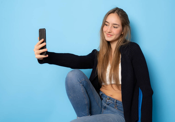 Pretty young happy woman making selfie on smartphone isolated over blue background. - Foto, immagini