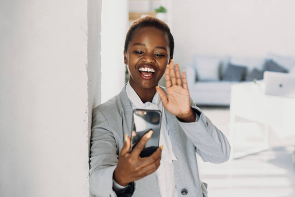 Mujer de negocios afroamericana hablando y saludando a la gente en videollamada en ssmartphone. - Foto, Imagen
