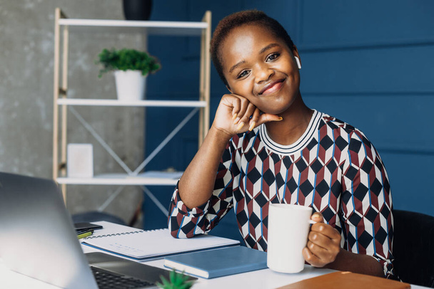 Afroameričanka sedící u laptopu a usmívající se při pohledu do kamery. Pauza. Obchodní žena. Koncept pracoviště. - Fotografie, Obrázek