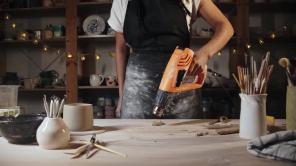 Young woman potter burns clay handle using an industrial dryer - Filmagem, Vídeo