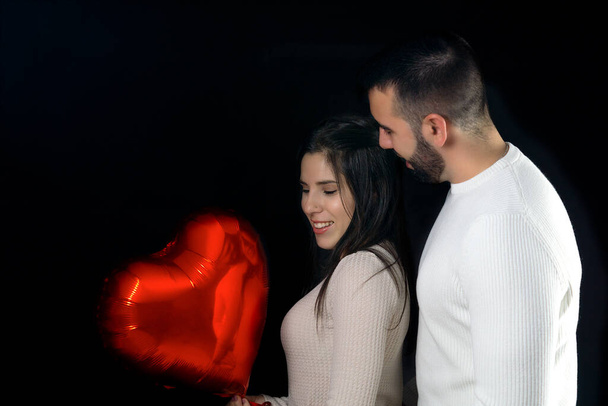 Jóvenes felices reflejados en un globo en forma de corazón en el día de San Valentín con un fondo negro. - Foto, imagen
