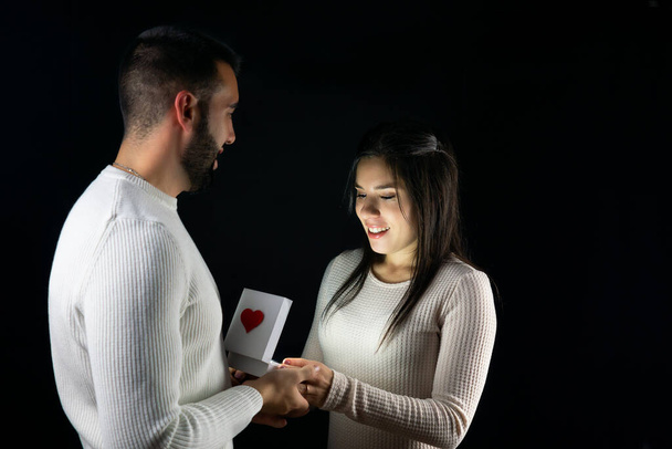 Ο άνθρωπος δίνει ένα δώρο στη γυναίκα του την ημέρα του Αγίου Βαλεντίνου με μαύρο φόντο. - Φωτογραφία, εικόνα