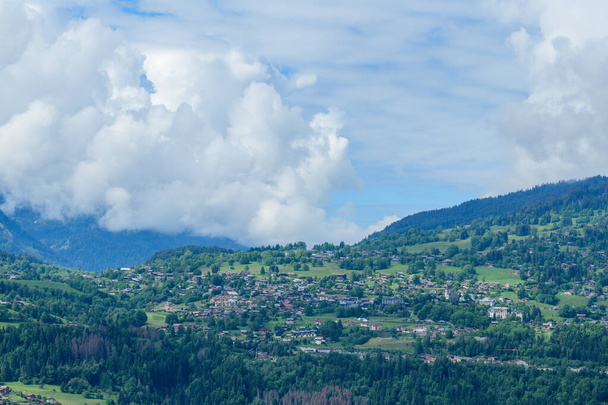 Αυτή η φωτογραφία τοπίου τραβήχτηκε στην Ευρώπη, στη Γαλλία, στις Άλπεις, προς το Chamonix, το καλοκαίρι. Βλέπουμε την πόλη Combloux στη μέση της υπαίθρου στο Mont Blanc Massif, κάτω από τα σύννεφα. - Φωτογραφία, εικόνα