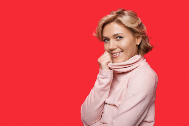 Closeup portrait of a smiling woman in sweater looking at camera isolated over pink background with copyspace. - Foto, Bild