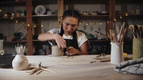 Young woman potter trying on a clay handle to a cup and looking over it - Video