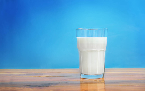 Glass of milk on wooden surface against blue background - Фото, зображення